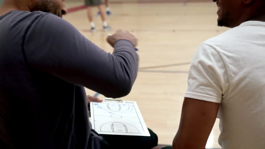 A coach and player fist bump as two team mates stand on the court