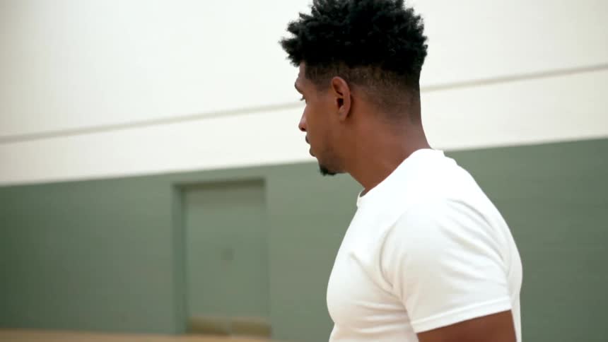 Two men walk in a gym as another man grabs a basketball