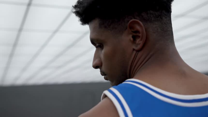 Black basketball player with blue jersey looks sideways in a basketball court
