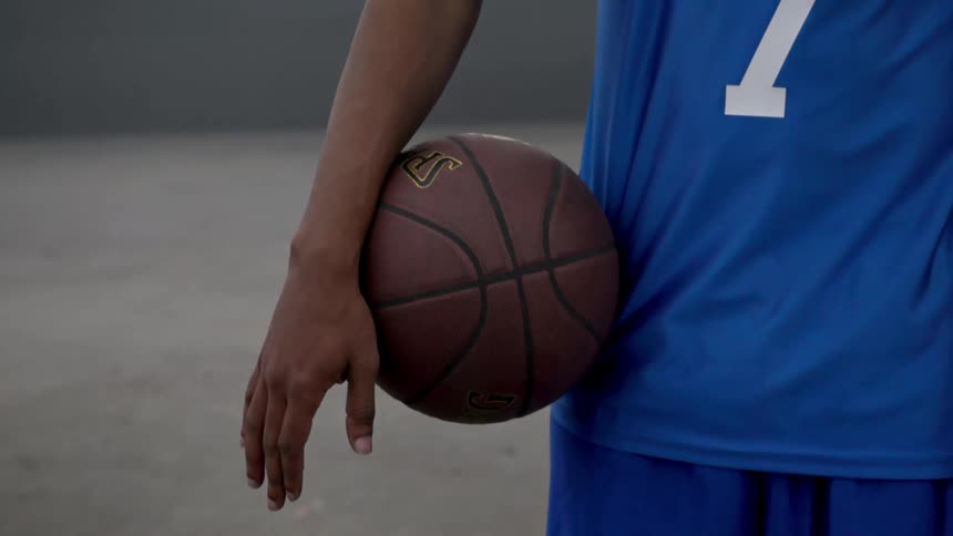 Man wearing blue basketball jersey holds basketball on his hip