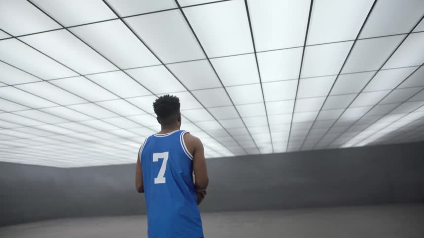 A black man with a basketball stands in a room where overhead lights flash