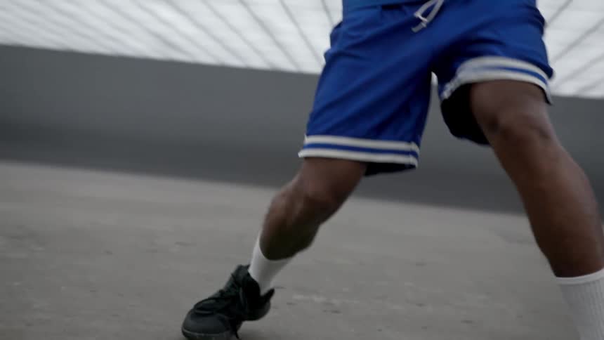 Man dribbles ball on grey concrete under mesh stretching overhead