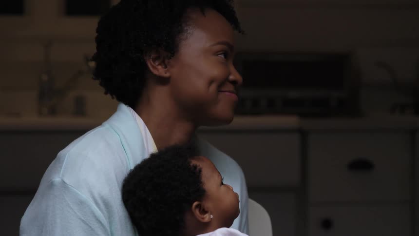 A woman sits in her kitchen with her baby on her lap and talks and laughs with someone