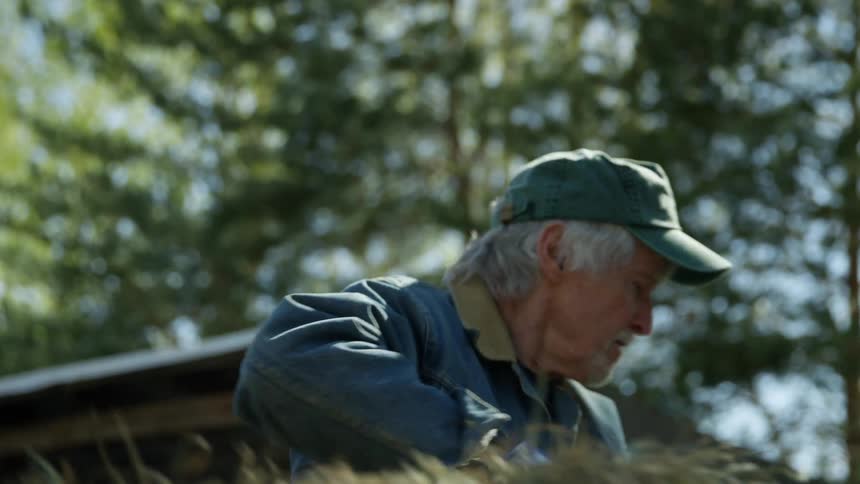 A farmer is outdoors carrying a bale of hay