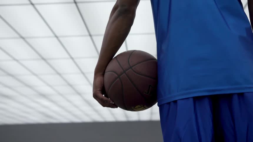 Basketball player wearing blue jersey and holding basketball stands under bright white ceiling tiles