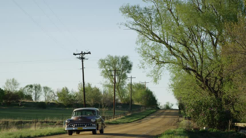 A red classic car drives on a dirt road in the countryside