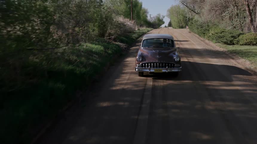 Vintage car driving along a dirt path in the country
