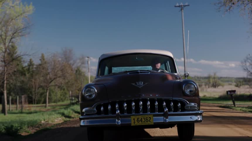 Elderly man drives a red classic car on a dirt road in the countryside