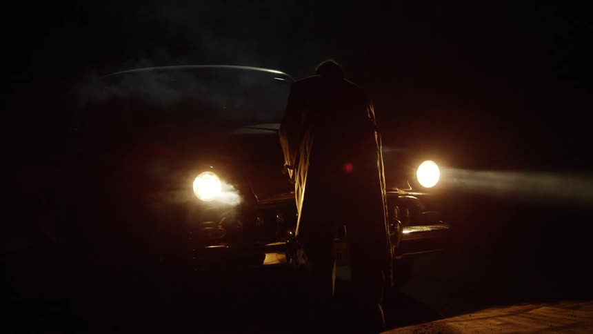 Man walking around and opening hood of classic car at night