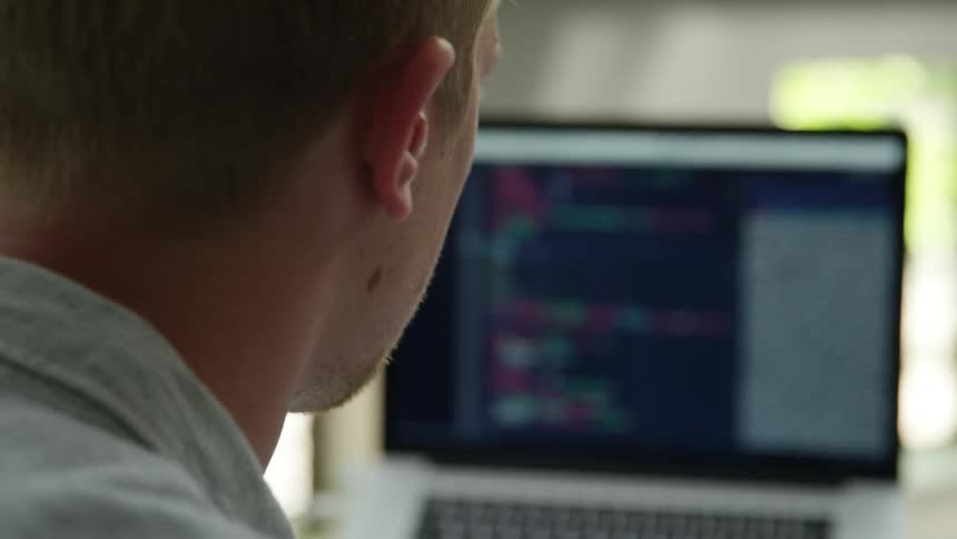 Man sitting at a desk looks at a laptop and takes notes