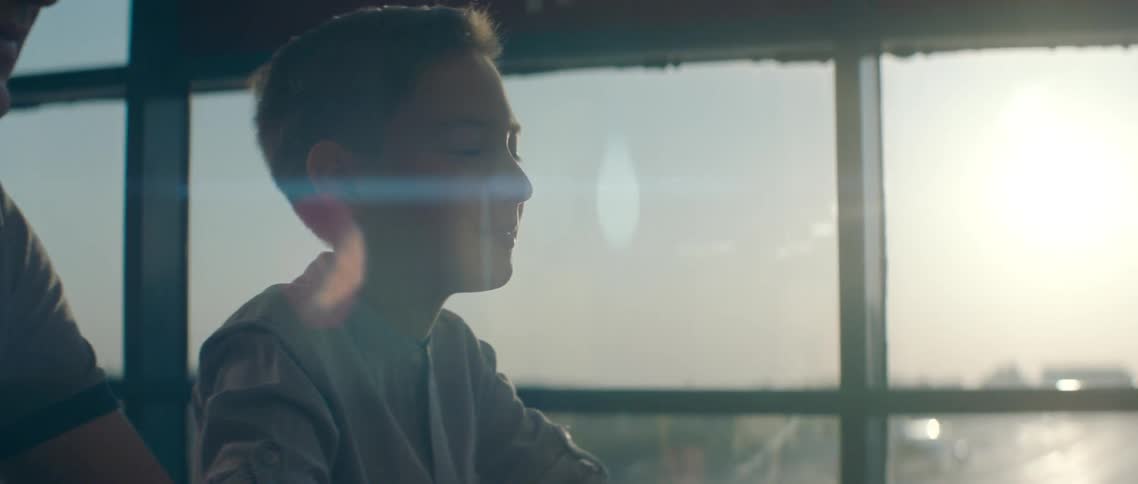 A boy sits with his parents at an airport and looks out the window