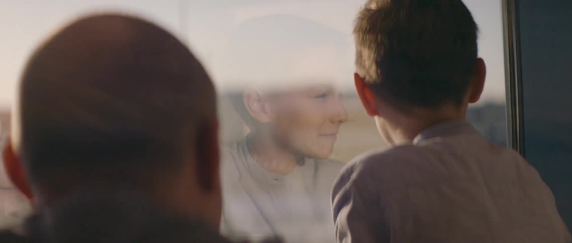 Man sits behind boy looking out window