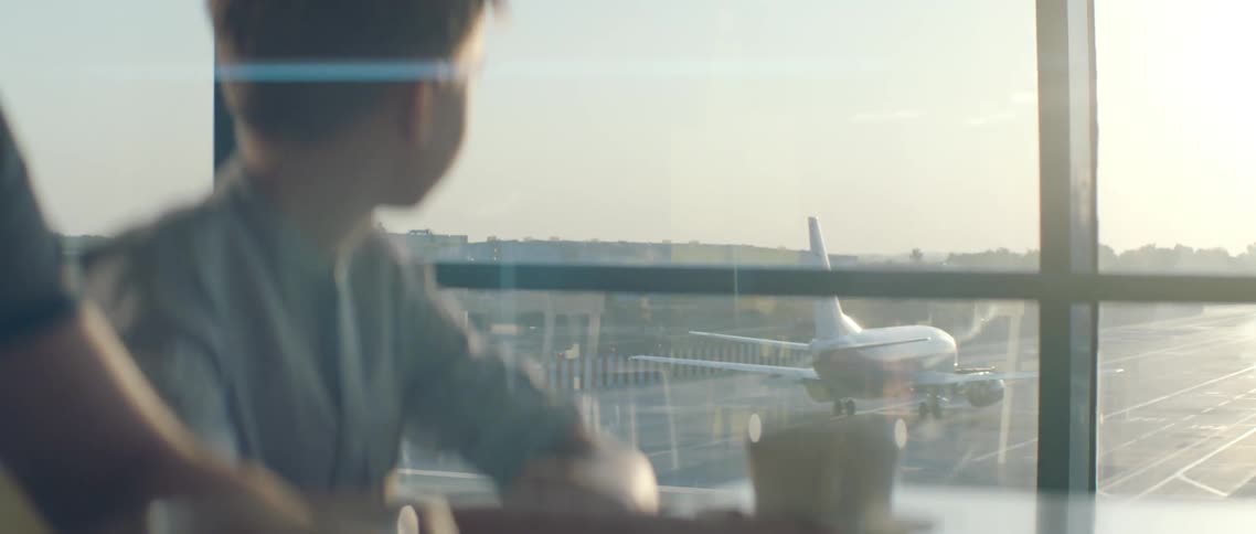 A boy looks out an airport window at an airplane
