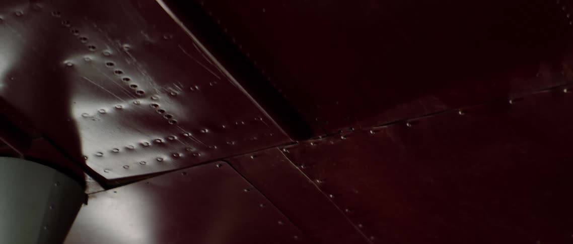 Light shines on a length of red metal with rivets