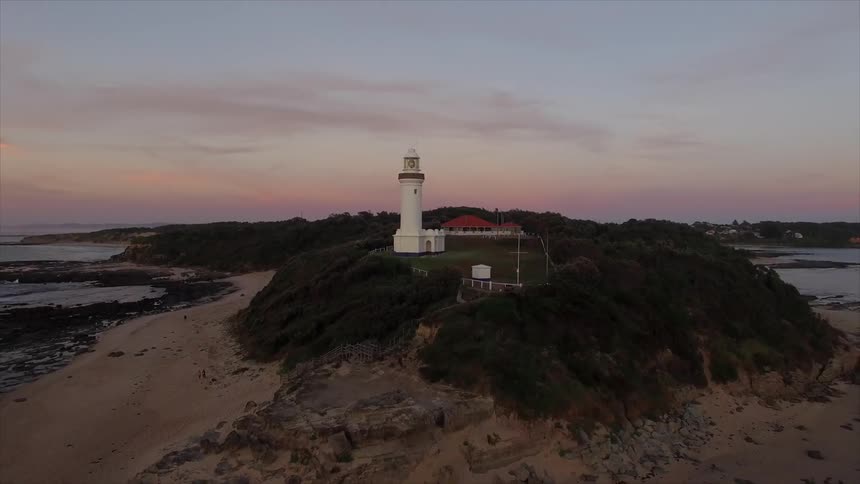 A large light tower sits near the shore at sunset