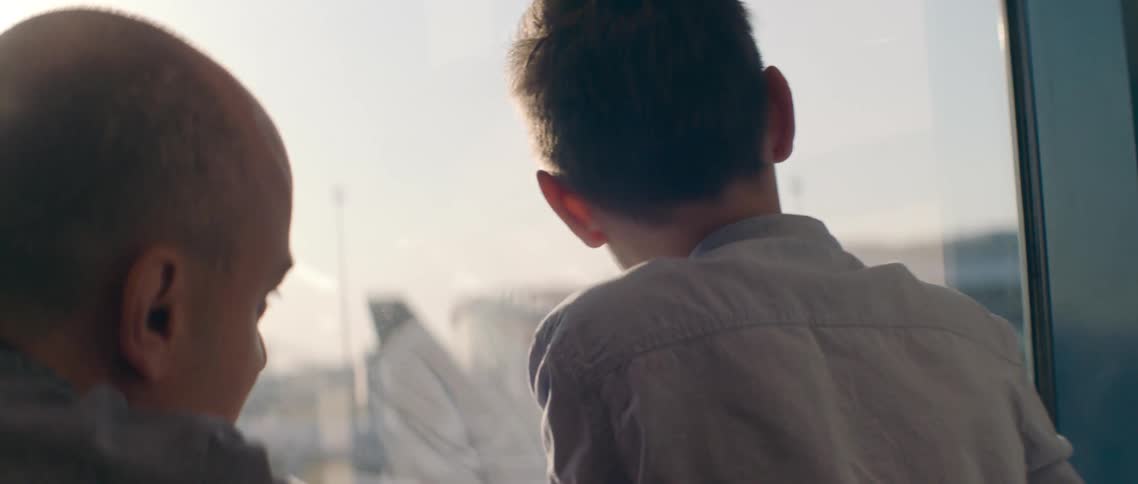 A father points out the window to his son as they talk
