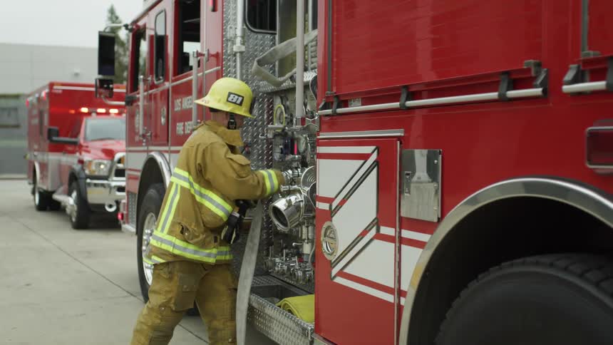 A fireman is connecting a fire hose to a firetruck in preparation to extinguish a fire