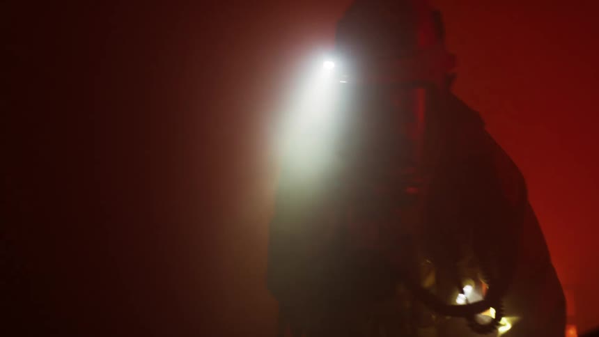 Firefighters wearing gear equipment walk through a smoke filled dark room