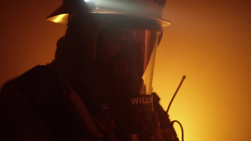 A fireman stands inside a building with a bright light behind him