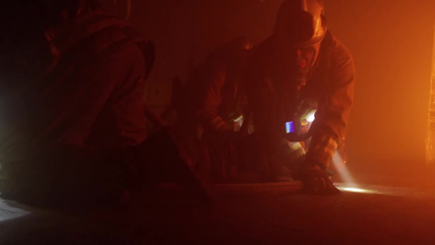 Fireman crawl low on the floor in thick smoke using flashlights