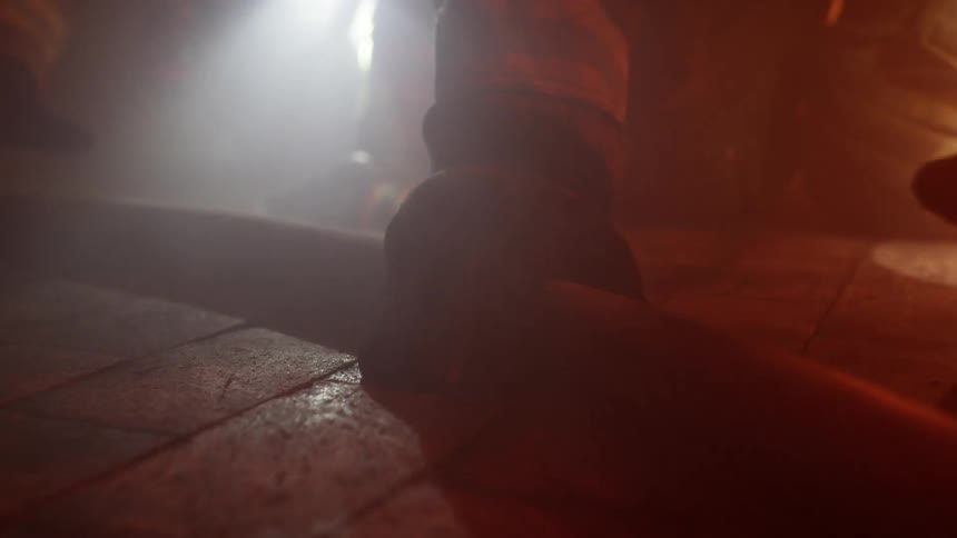 Firefighters crawl on the floor of a building and reach for a hose