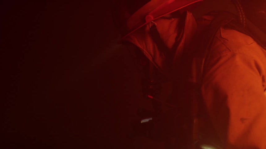 Two firefighters crawl using a hose for guidance inside of a dark structure