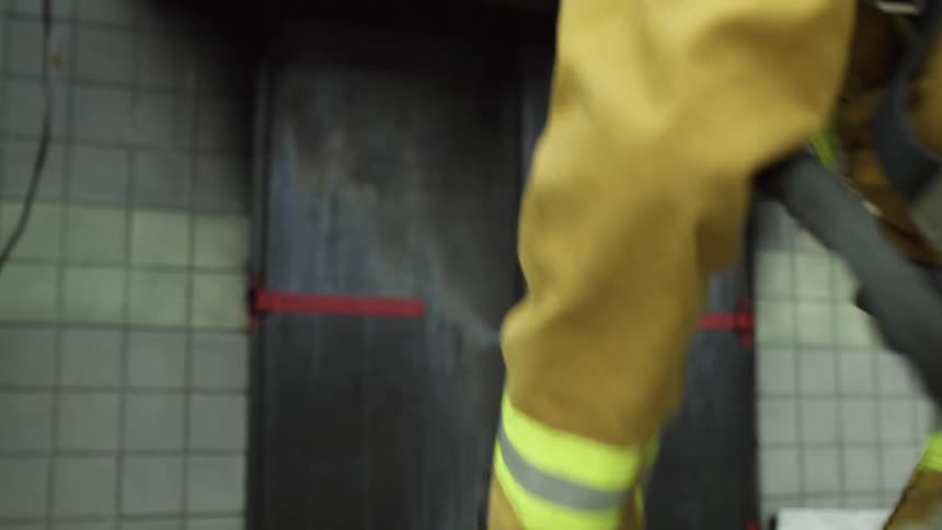 A firefighter runs up to a building and sets a hose on the ground