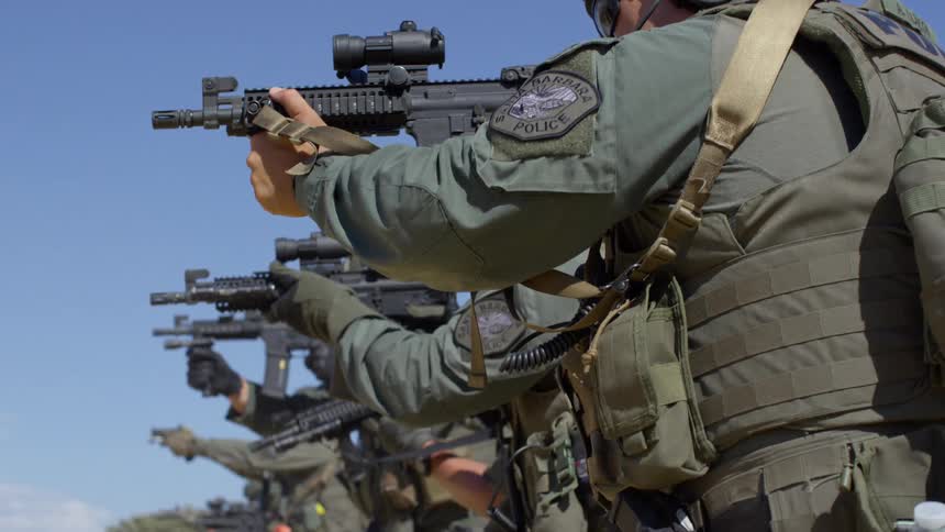 Military personnel in a line as they practice shooting their rifles outdoors