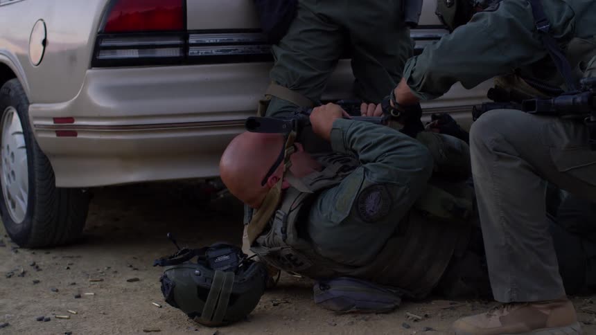 Field medic helps a downed soldier behind a car in a training exercise
