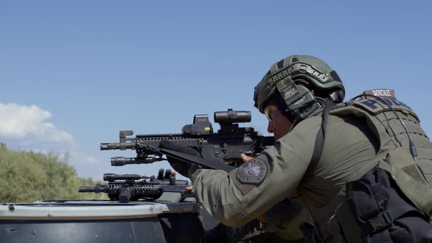 Two soldiers shelter behind black barrels aiming rifles