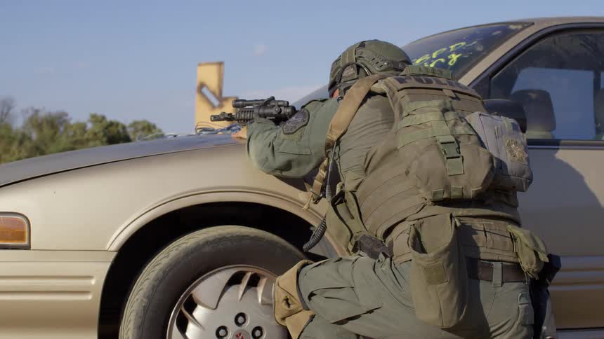 A soldier hides behind a car as he shoots his gun