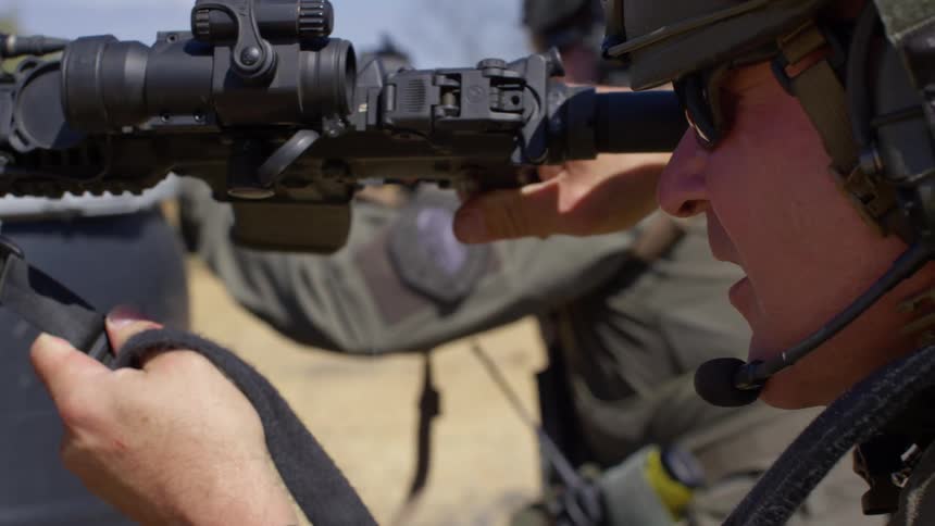 Men aiming rifles shoot over black barrels their weapons are propped on