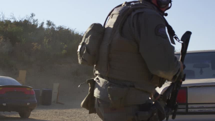Two military police run and take cover behind a car and then shoot their rifles
