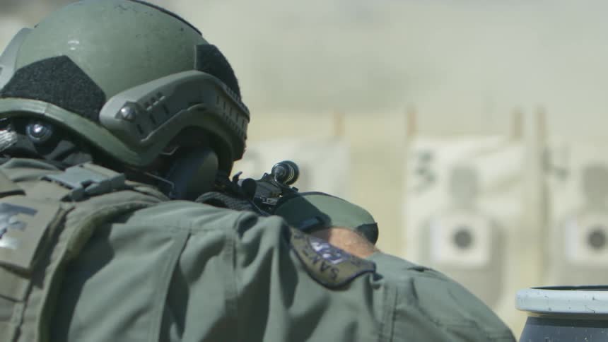A person with a helmet gloves and uniform shooting a rifle