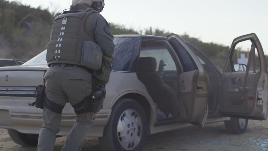 A soldier jumps out of a car and runs behind it and fires his gun