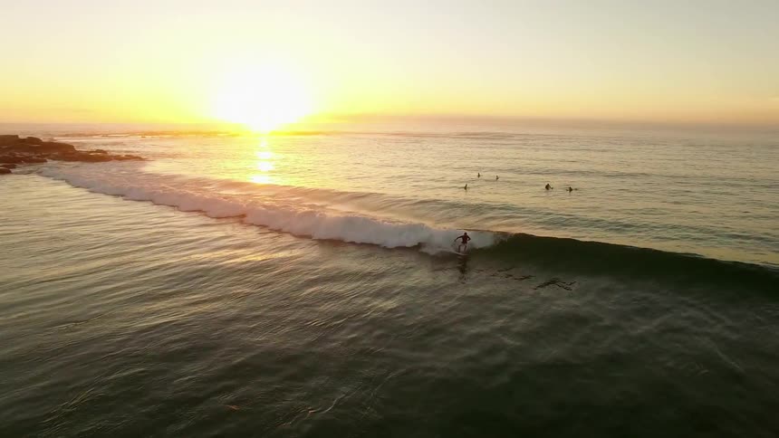 Surfers are in the water of a beach as the sun sets