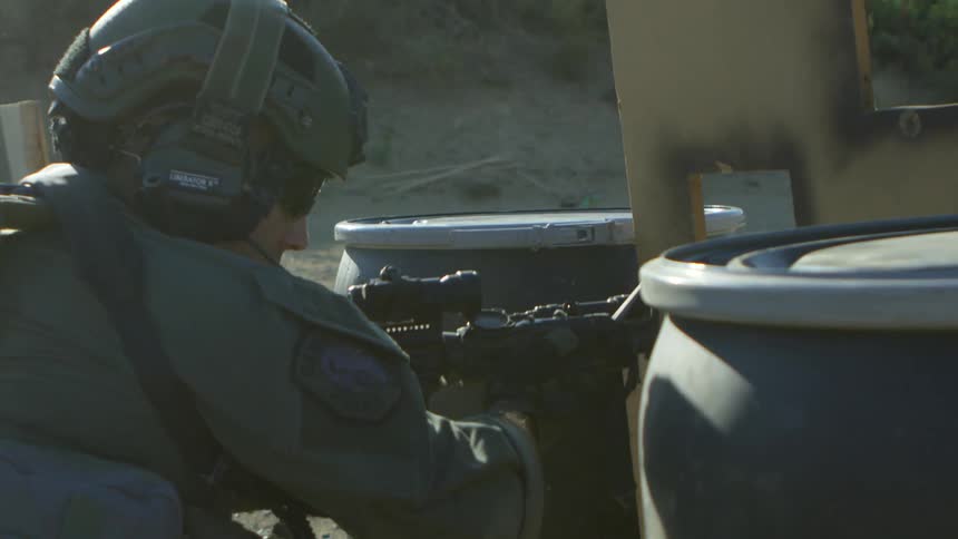 Police officer in military gear shoots an assault rifle while taking cover on a training exercise