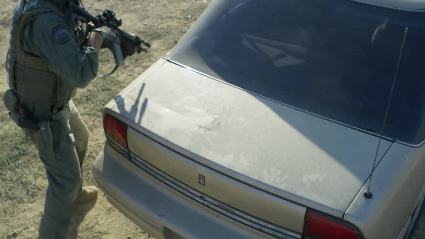 An armed soldier hides behind a vehicle and shoots his weapon