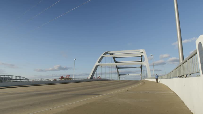 Man walking over an arched bridge under a blue sky