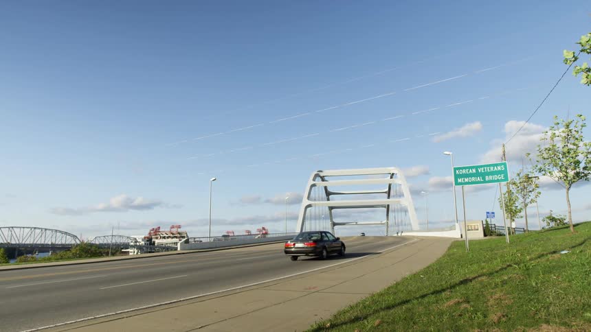 Car approaches and crosses bridge passing road sign and trees