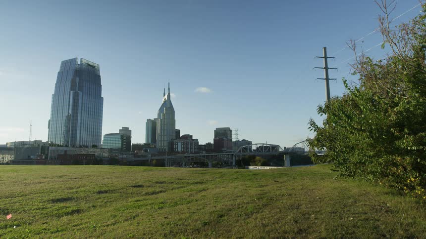 A park with grass and bushes sits near a bridge running into the downtown area of a city