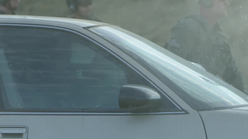 Three soldiers outside of a car and two inside that are shooting bullets through the windshield