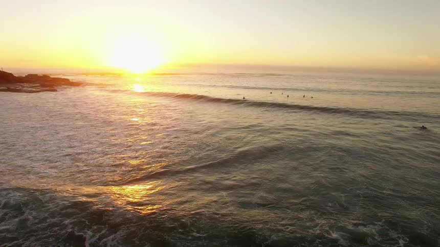 The sun is setting as people surf in the ocean