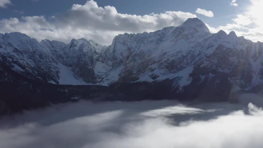 A snow covered mountain ridge surrounded by clouds both above and below