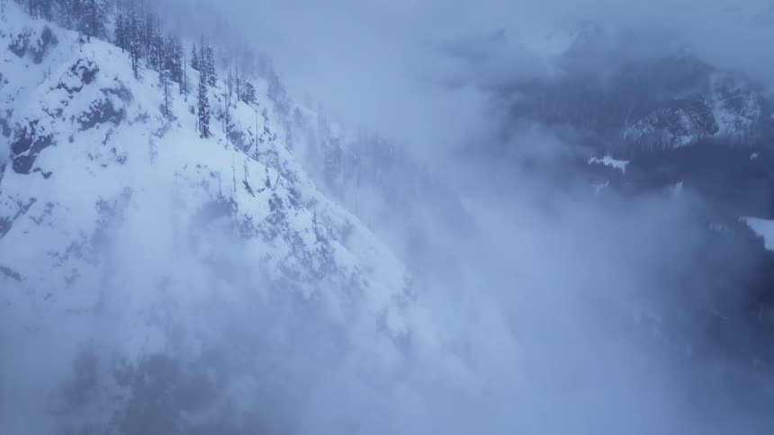 A cloudy haze hangs over snowy mountains and a valley