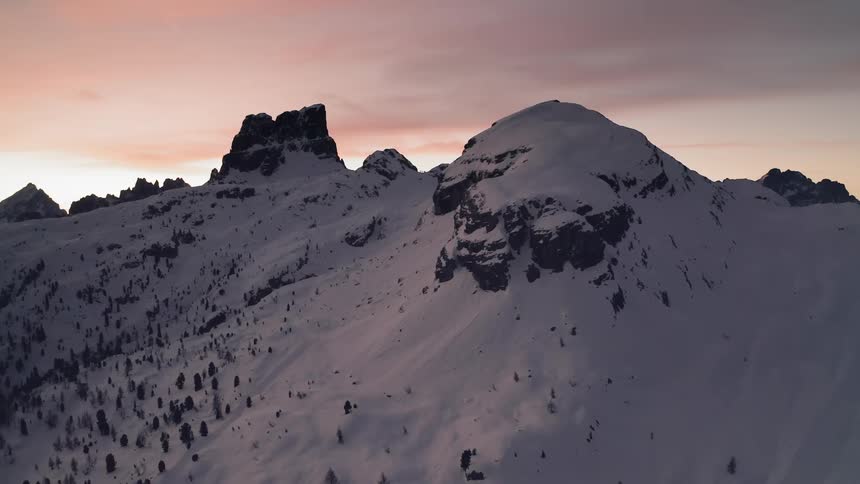 Aerial view of a snow capped mountain and a mountain slope with trees against red sky
