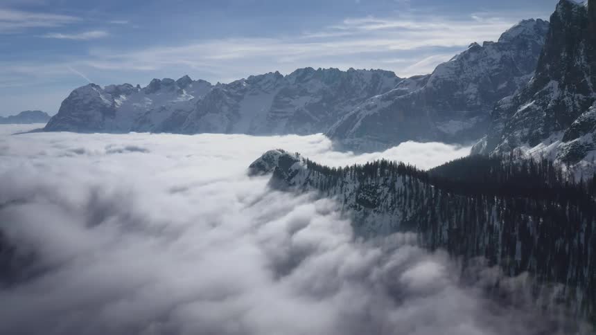 Mountain forest trees and rocky ridges stick out above a thick cloud layer with a blue sky above