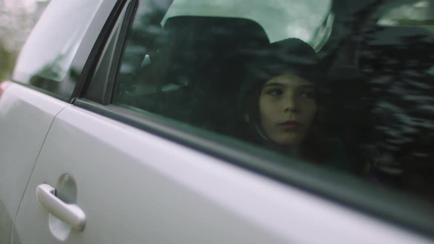 A child sits in the backseat of a car and looks about