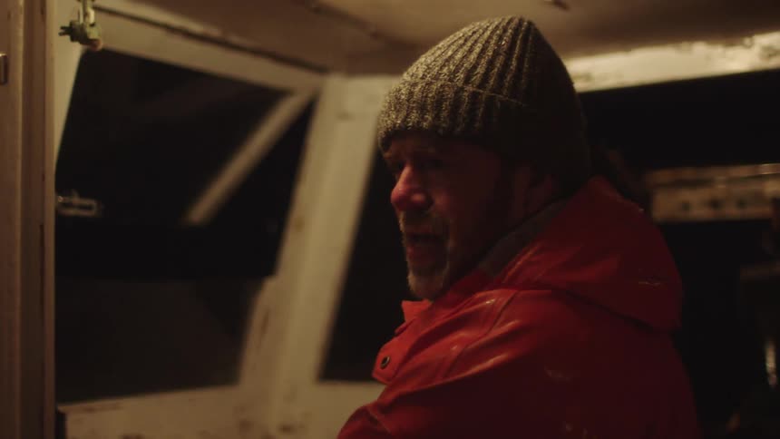 A boat captain wipes the rain and water off his face as he travels at night