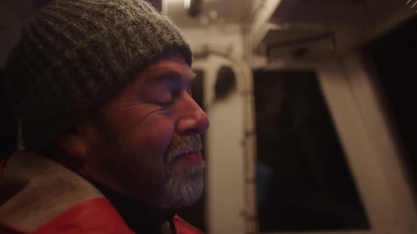 A fisherman stands in front of a computer on his boat